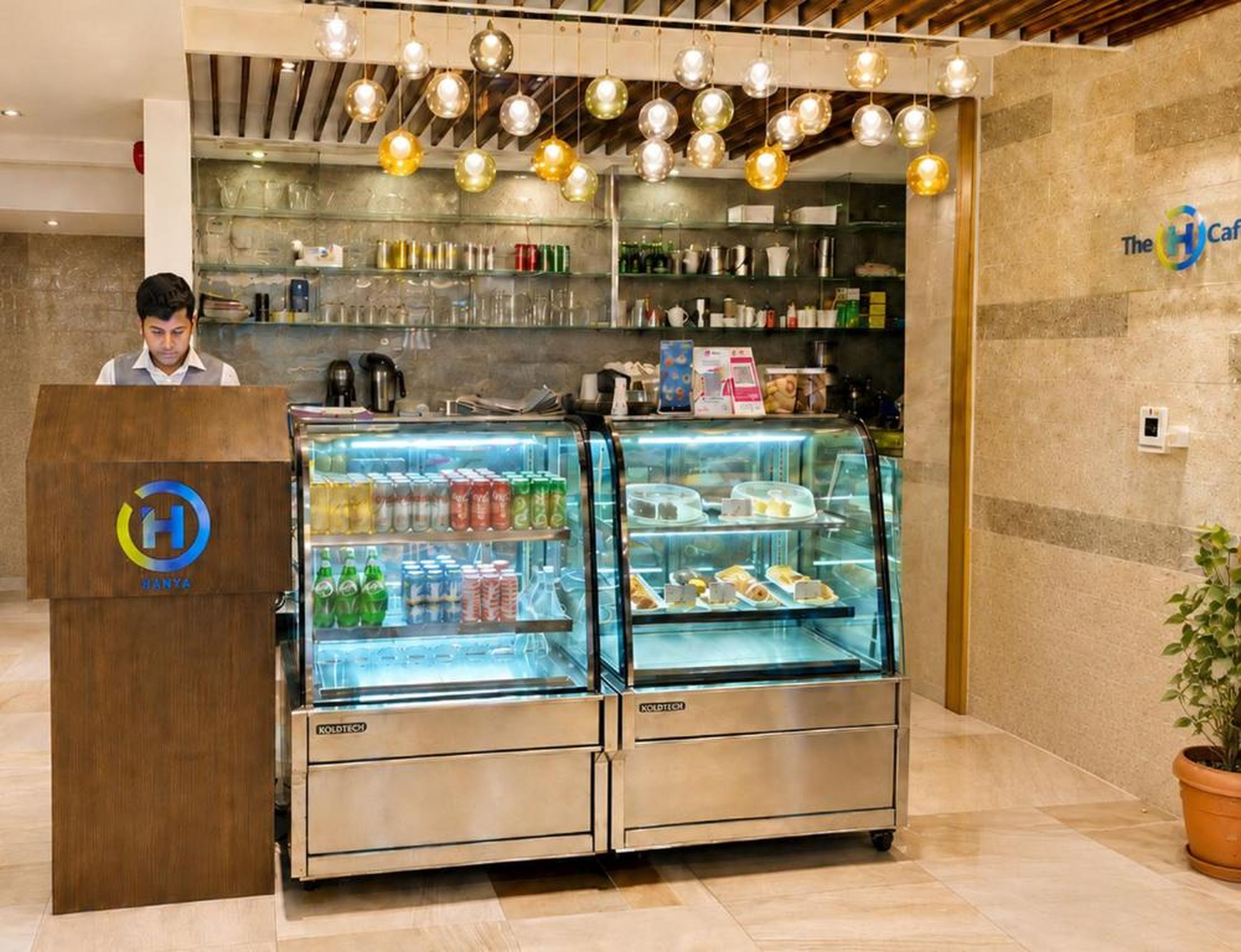 Zona de recepción de un hotel con un expositor de vidrio que contiene bebidas y un atril con un logotipo.