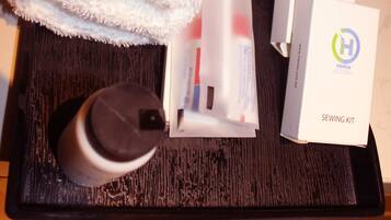 A neatly arranged bathroom with a white towel, a sewing kit, and a sanitary bag on a tray.