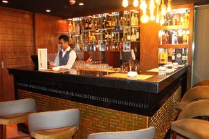 Un espace bar avec un comptoir, des étagères remplies de bouteilles et des tabourets de bar.