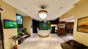 A hotel lobby with a reception desk, sofas, a TV, and a chandelier. - HANSA - A Premium Residence (Dhaka)
