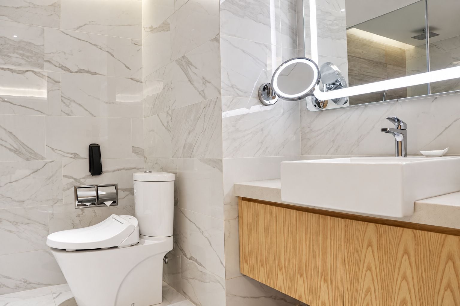 A modern bathroom with a toilet, sink, mirror, and marble tiles.