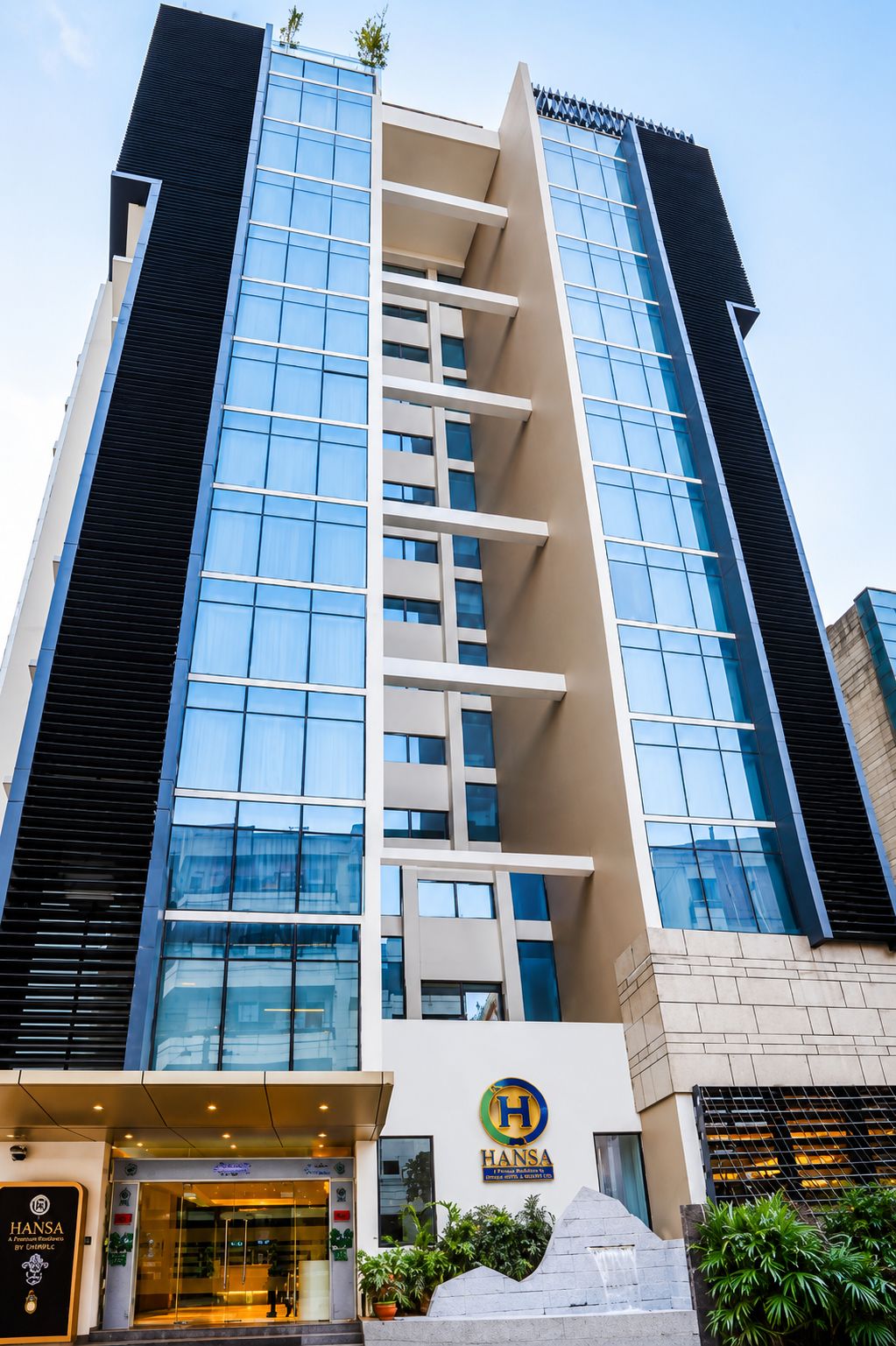 A modern hotel building with a prominent Hansa logo, a glass facade, and a water feature at the entrance.