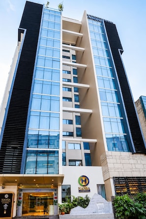 Un hôtel moderne, reconnaissable à son logo Hansa bien visible, à sa façade en verre et à un élément décoratif aquatique situé à l’entrée.