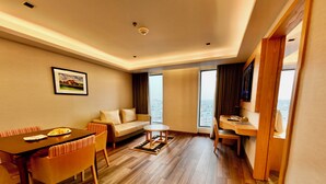 A modern hotel room with a dining area, a sofa, a small table, and a view of the city. - HANSA - A Premium Residence (Dhaka)