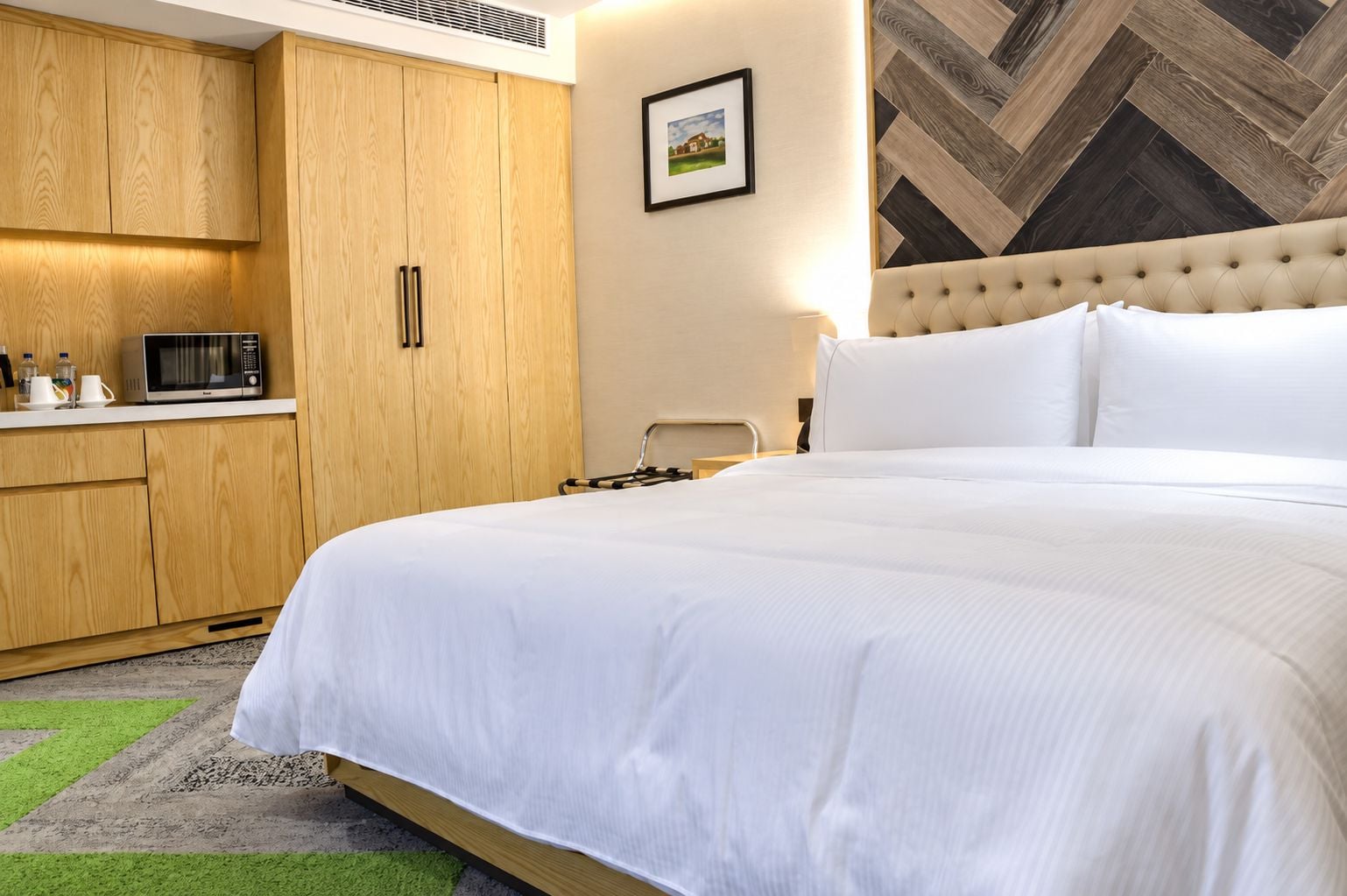 Habitación de hotel con una cama grande, un armario de madera, un microondas y una pared con estampado pata de gallo.
