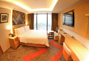 Quarto de hotel com uma cama grande, uma escrivaninha, uma televisão e vista para a cidade.
