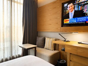 A hotel room with a bed, a desk, a television mounted on the wall, and a window with curtains. - HANSA - A Premium Residence (Dhaka)