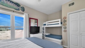 A hotel room with a large bed, a TV on a bedside table, a bunk bed, and a view of the beach. - Gorgeous 4 Bdrm, 3 Ba Gulf Front Private Home, Sleeps 10 (Gulf Shores)