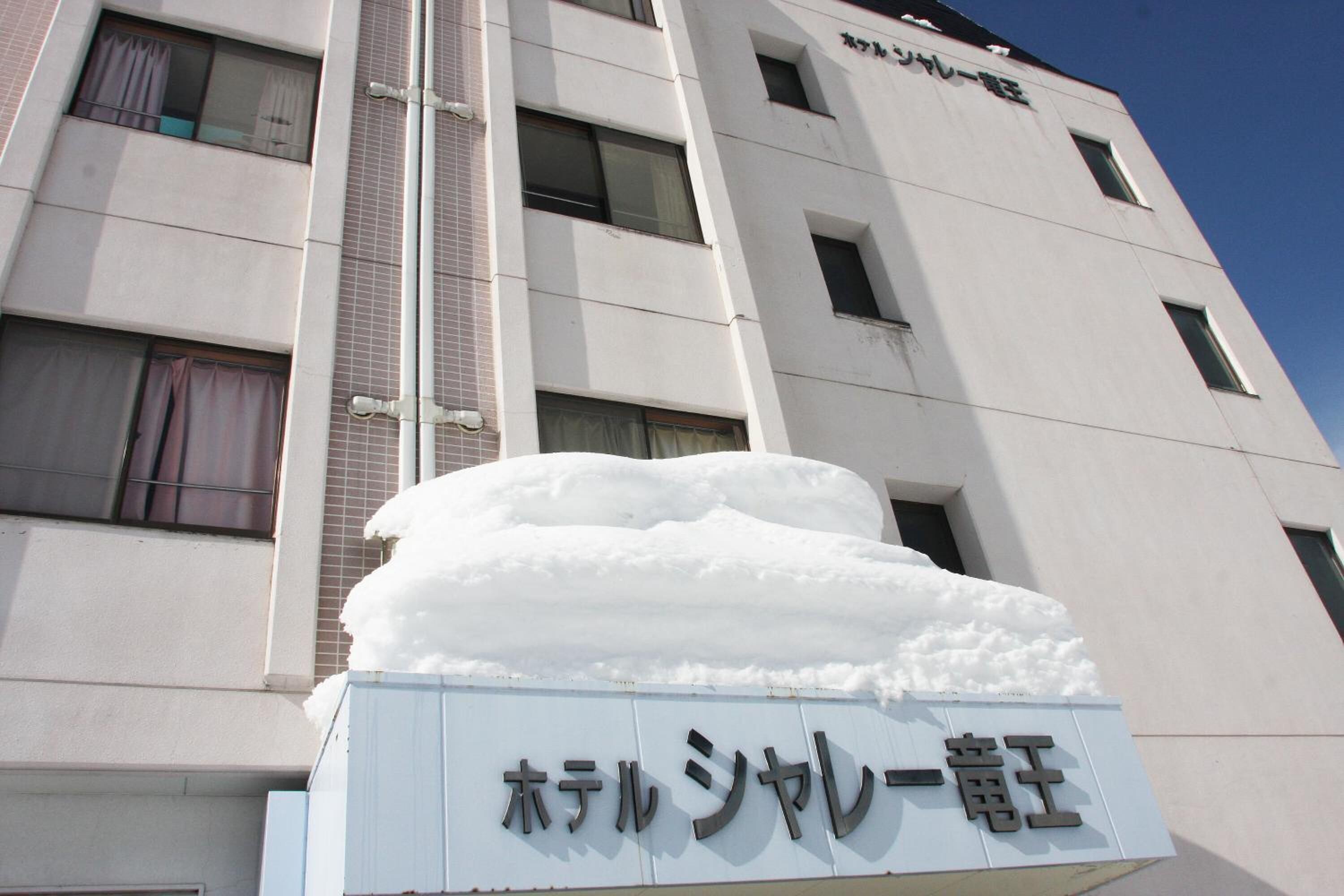 A hotel building with a sign that reads "ホテル シャレー電気" and a large snow pile in front.