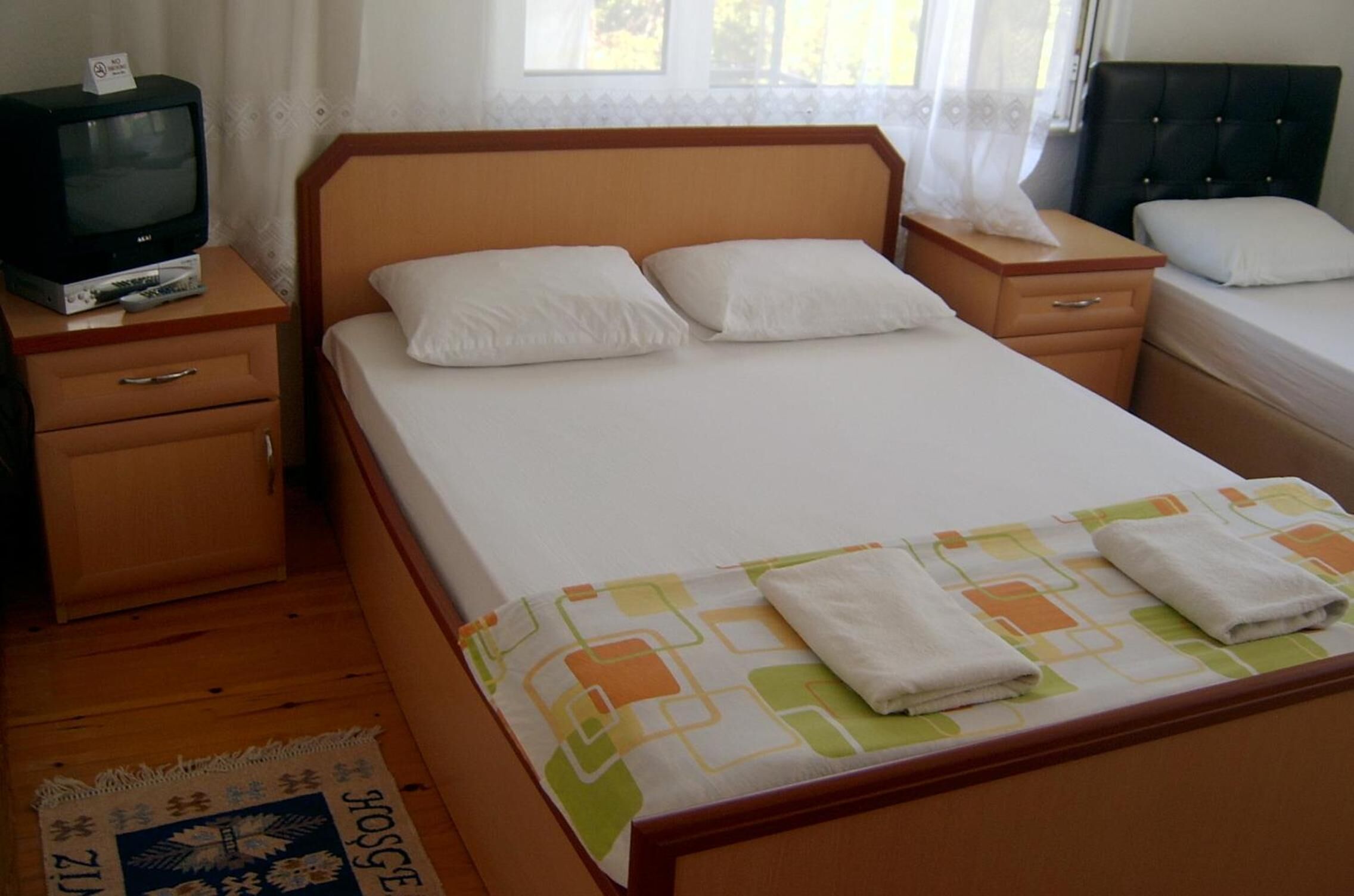 Un lit simple avec une tête de lit en bois, une table de chevet avec un téléviseur et une petite commode.