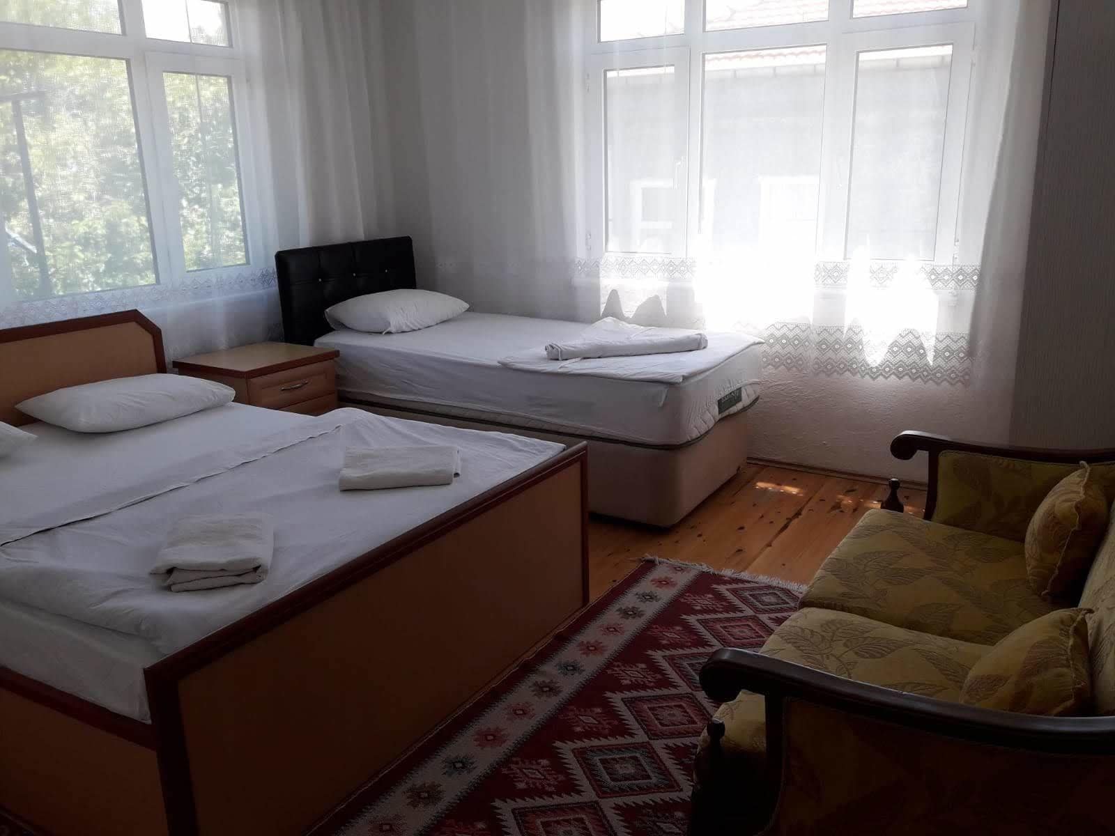 A room with two beds, a wooden floor, a patterned rug, and a chair.