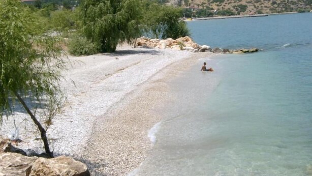 Una playa de guijarros con agua cristalina y una persona sentada en la orilla.