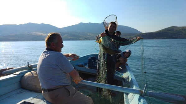 A boat with a person holding a fish, another person sitting, and a child on the deck. - Sehsuvar Peace Pension (Egirdir)