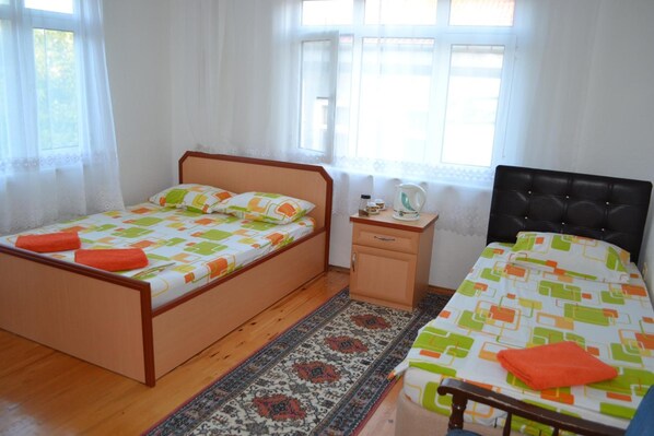 Un dormitorio con dos camas, una mesita de noche pequeña, una mesita auxiliar y una ventana con cortinas.