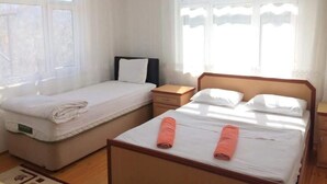 Una habitación con dos camas, cabecero de madera, mesita de noche y ventana con cortinas.
