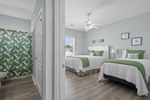 A bedroom with two beds, a ceiling fan, and a view of the outdoors.
