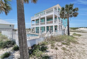 A multi-story beachfront property with a pool, white railings, and a view of the beach.