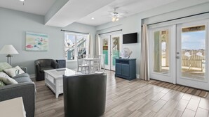 A spacious living room with a sofa, a coffee table, and a TV mounted on the wall. There is a staircase leading to an outdoor area with a view of the sea. - Luxury 6 Bdrm/6 Ba Gulf Front w/Private Pool and Great Views (Gulf Shores)