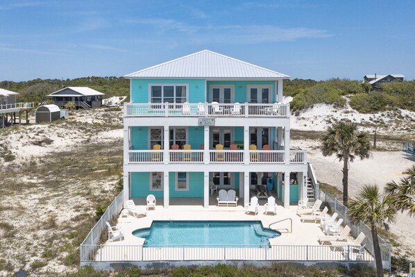A two-story beachfront house with a swimming pool, multiple balconies, and beachside views.