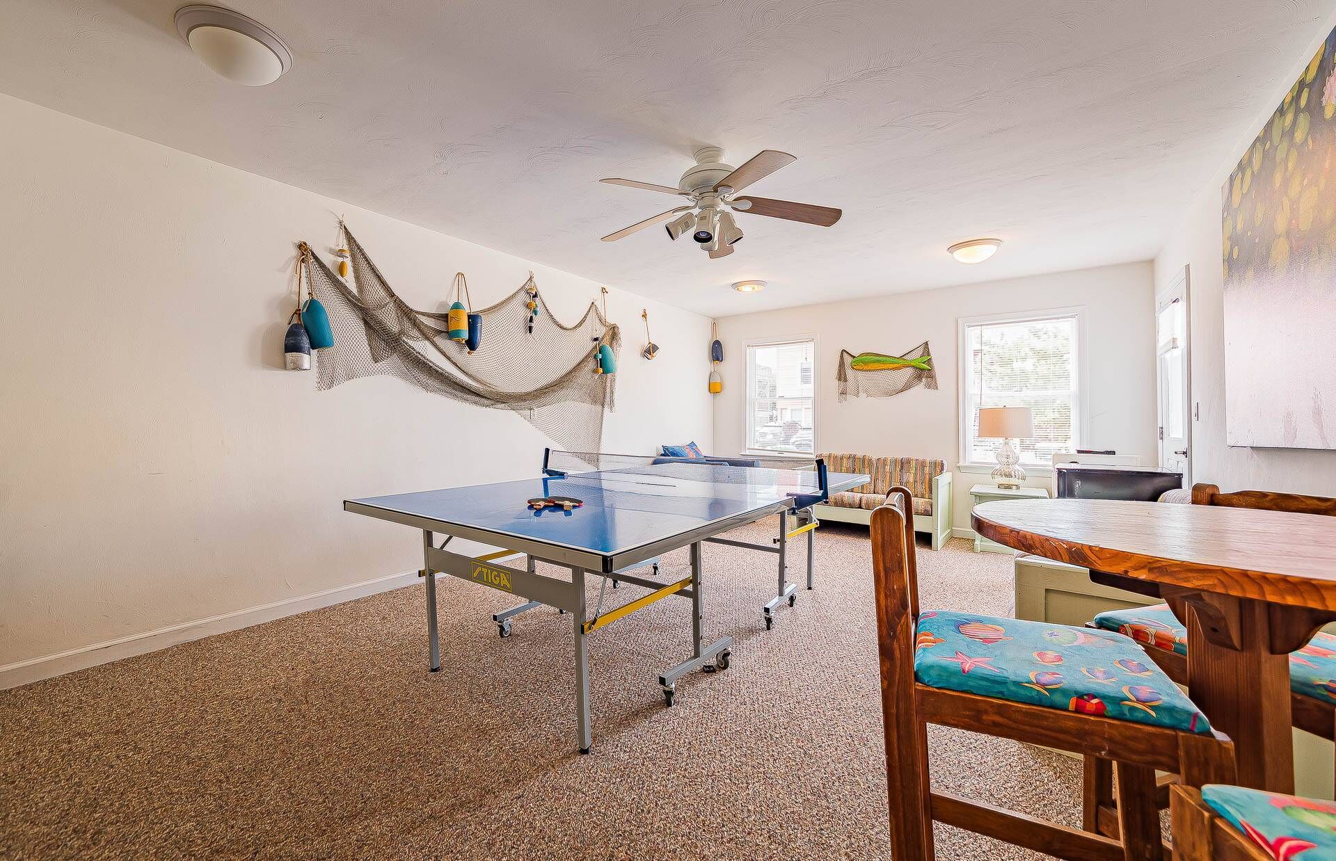 A room with a ping pong table, a ceiling fan, and a hammock.