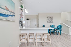 Une cuisine moderne avec des meubles blancs, un plan de travail blanc et un coin repas avec des chaises bleues et une table blanche.