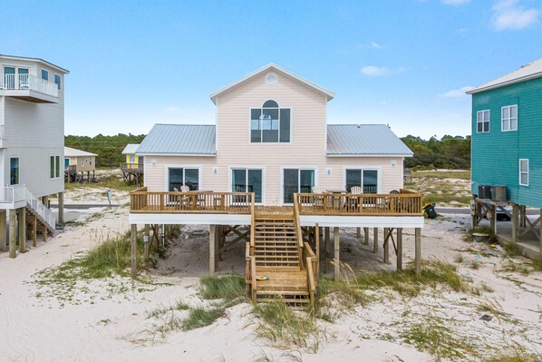 Une maison située en bord de mer, dotée d’une terrasse en bois et de nombreuses fenêtres.