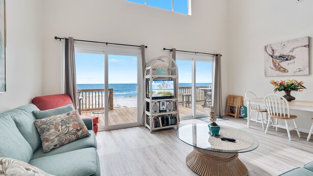 Een ruime woonkamer met een grote glazen deur die leidt naar een balkon met uitzicht op het strand.
