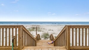 Een houten looppad dat naar een strand leidt, met een helder uitzicht op de oceaan.