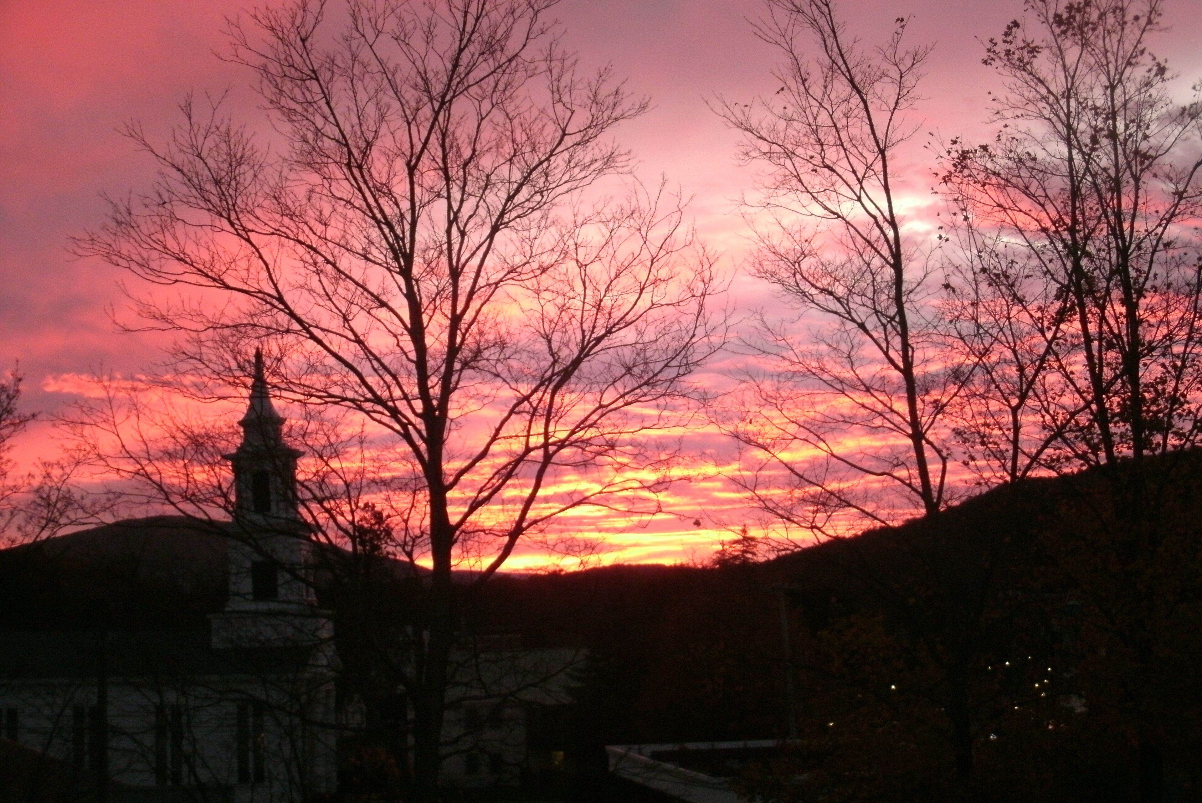 A sunset with a church silhouette and bare trees.