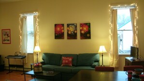 A living room with a green sofa, two lamps, a small table with a keyboard, and three paintings on the wall. - TOWNHOUSE-Slp 8 Mt View/6 BEDS. Downtown Windham. Walk to restaurants and stores (Windham)