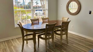 A dining area with a round table and four chairs, a chandelier, a large window with blinds, and a mirror on the wall. - Surfside Area Vacation Home Awaits (Cape Coral)