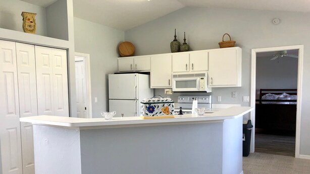 A modern kitchen with white cabinetry, a central island, a microwave, and a refrigerator. - Surfside Area Vacation Home Awaits (Cape Coral)