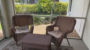 A covered porch with wicker furniture and a view of a house and greenery. - Surfside Area Vacation Home Awaits (Cape Coral)