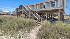 Ein Strandhaus mit einer Holzterrasse und einer Treppe zu einem Balkon.