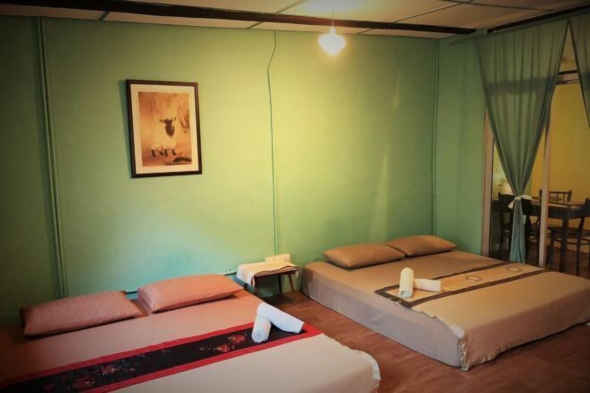 Une chambre avec deux lits, une petite table, une chaise et un tableau accroché au mur.