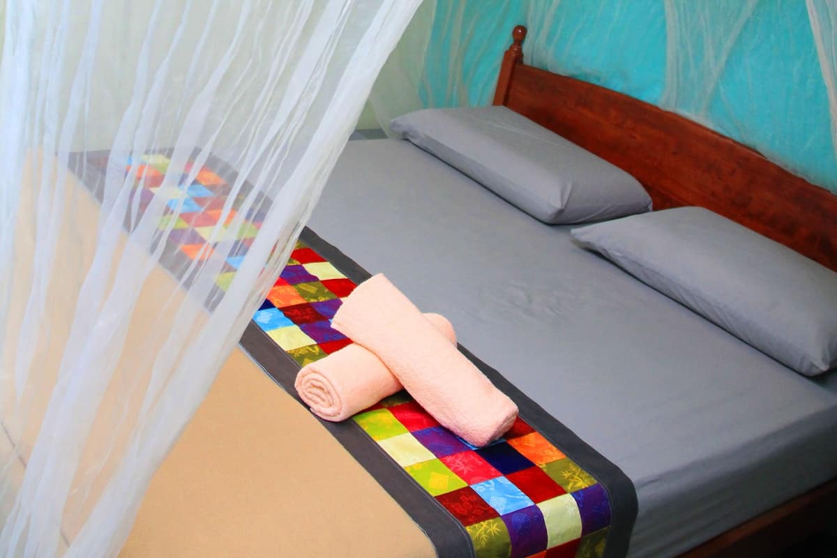 Un lit avec une couverture aux couleurs vives, une serviette enroulée et une tête de lit en bois.