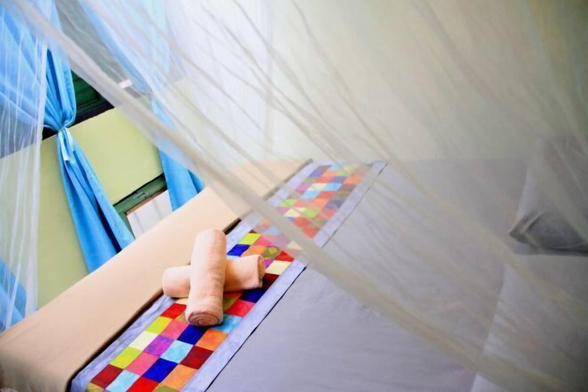Une chambre avec un lit, une couverture aux couleurs vives et une moustiquaire.