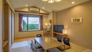 Une chambre d’hôtel dotée d’une grande fenêtre, d’une table à manger, de chaises, d’un téléviseur et d’un bureau avec une lampe.