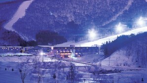 Un paysage enneigé avec un bâtiment doté de nombreuses fenêtres et une piste de ski en arrière-plan.