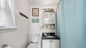 A small bathroom with a toilet, sink, and vanity. There is a framed picture on the wall and a sign that says "Happiness is the sand between my toes and the sunburn on my nose." - Cute beach house w/ramp for easy access. 3Bd/2Ba- Great Gulf Views/easy access. (Gulf Shores)
