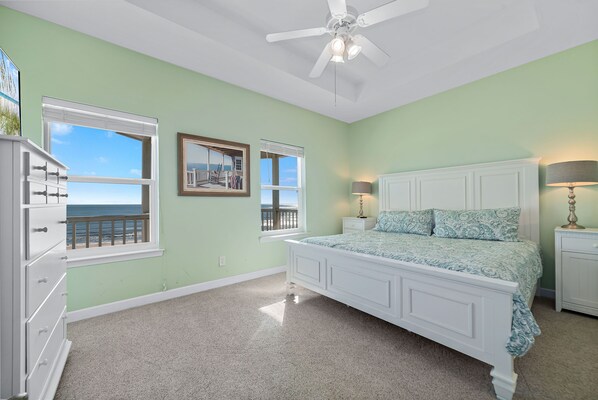 A bedroom with a bed, dresser, and windows with a view of the ocean.