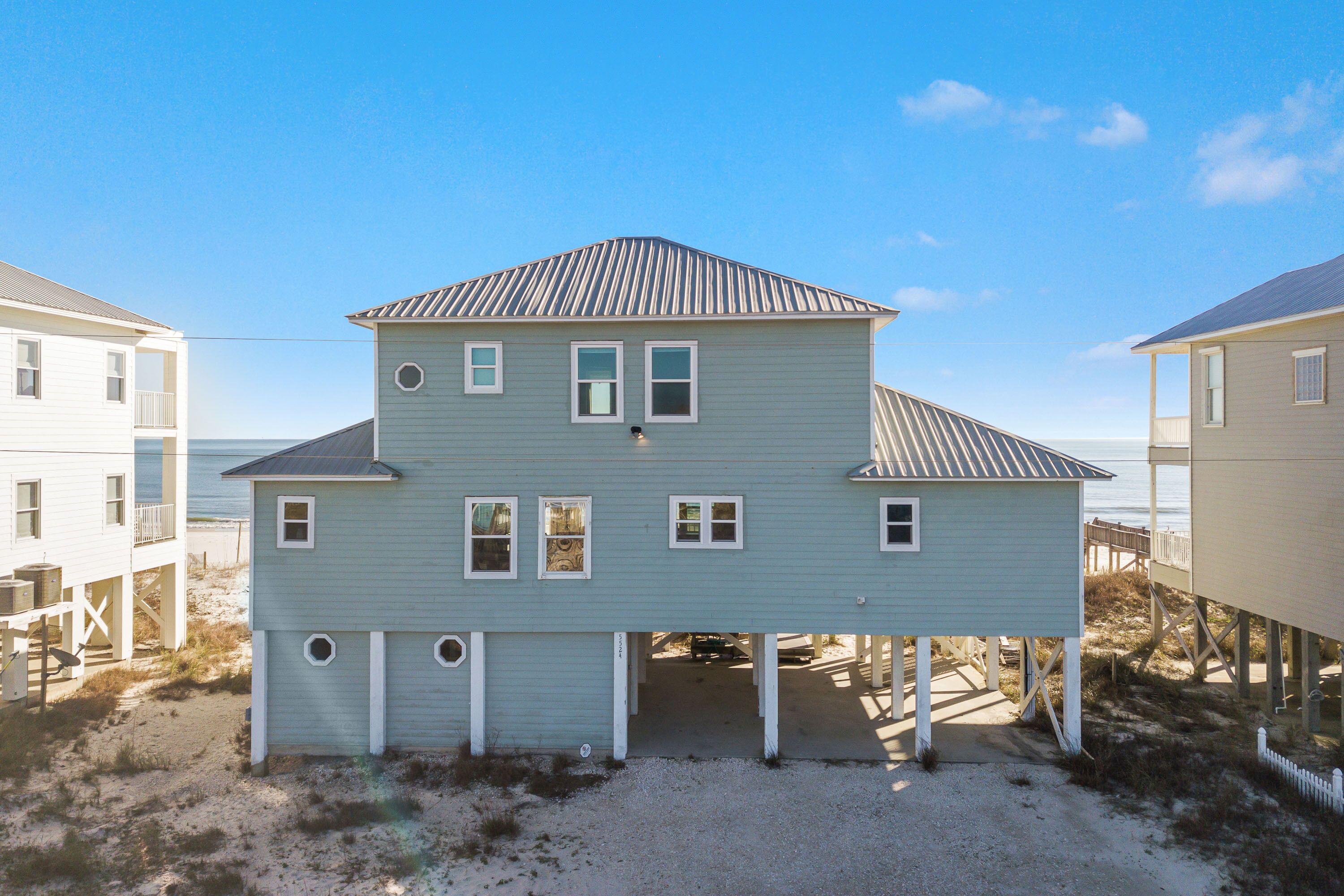Une maison à deux étages avec un toit à pignon, un porche avant couvert et une plage de sable en arrière-plan.