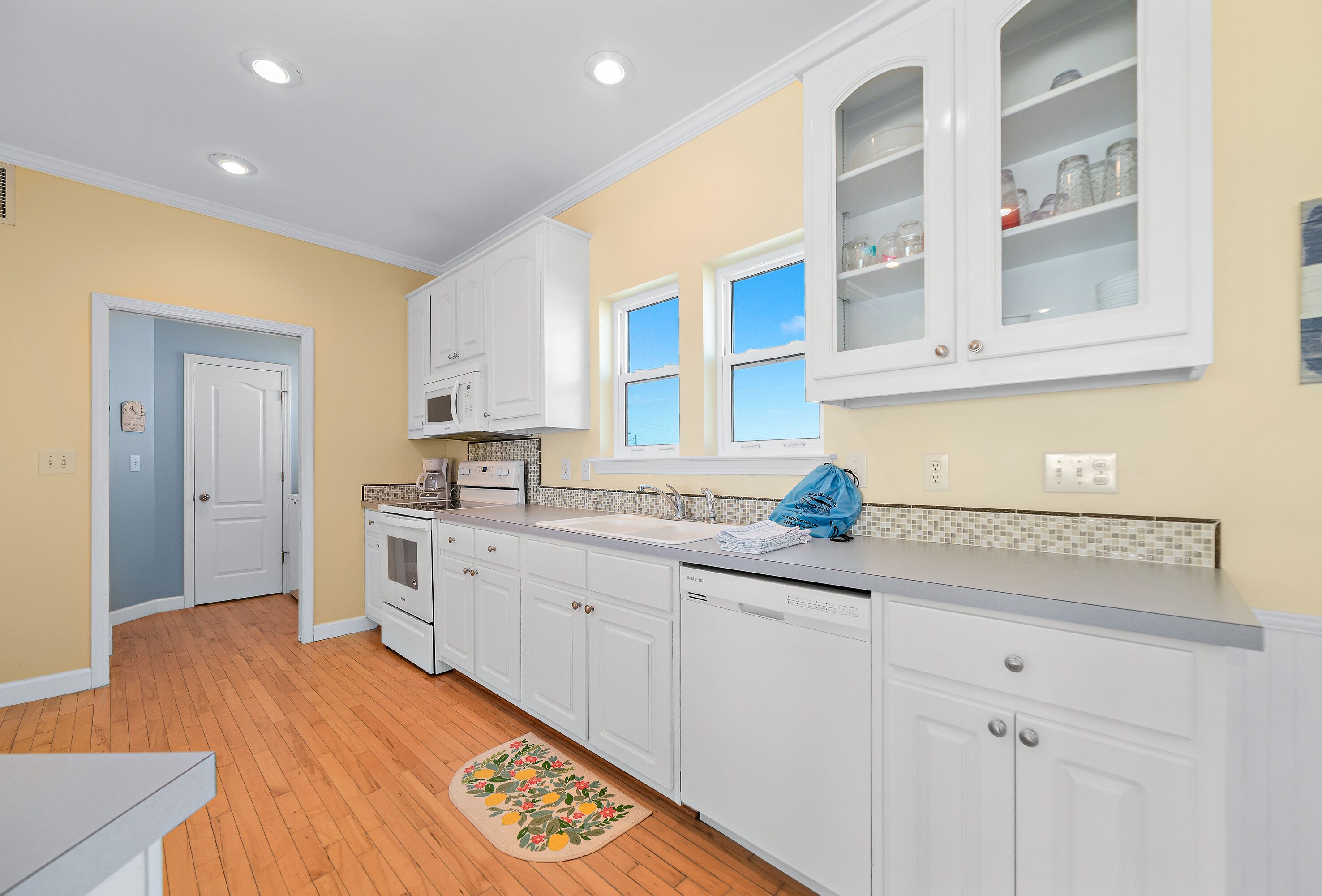 A kitchen with white cabinets, a microwave, and a dishwasher. There is a window above the sink, and a door leading to another room.