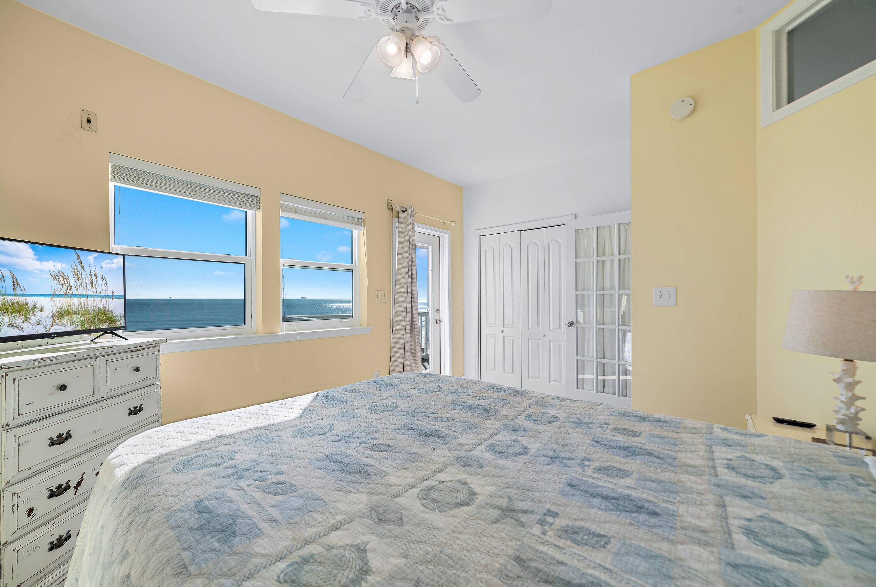 A bedroom with a large bed, a ceiling fan, a dresser, and a TV.