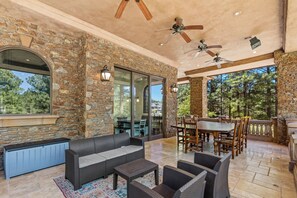 An outdoor patio with stone walls, a sofa, dining table, chairs, and ceiling fans. - The Castle – Luxury Northern Arizona Estate | Sleeps 17 (Flagstaff)
