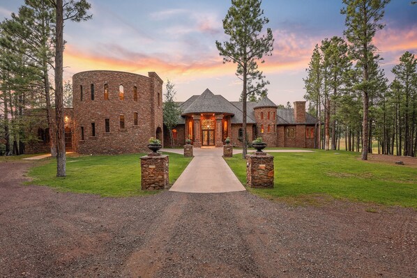 A large, stone mansion with a central tower and a circular building, surrounded by a well-maintained lawn and tall trees. - The Castle – Luxury Northern Arizona Estate | Sleeps 17 (Flagstaff)