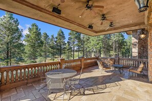 A covered outdoor patio with stone flooring, metal furniture, and a view of a forest. - The Castle – Luxury Northern Arizona Estate | Sleeps 17 (Flagstaff)