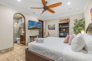 A bedroom with a bed, a ceiling fan, a bathroom with a toilet and shower, and a bookshelf. - The Castle – Luxury Northern Arizona Estate | Sleeps 17 (Flagstaff)