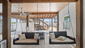 A covered outdoor seating area with two wicker swings, a ceiling fan, and a view of the surrounding landscape.