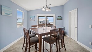 A dining area with a large wooden table and chairs, a chandelier, and artwork on the walls.